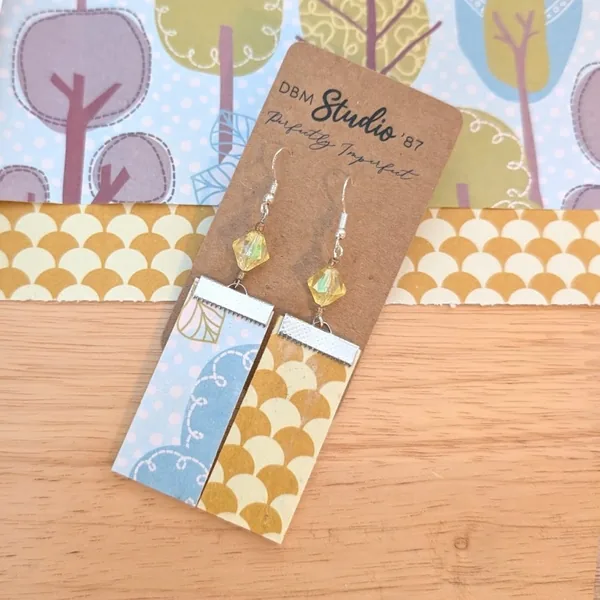 Medium rectangle dangle scrapbook paper earrings. silver metal accents and yellow clear crystal shaped beads. Front is light blue with trees and back is gold/yellow fan shaped. Lightweight Mo